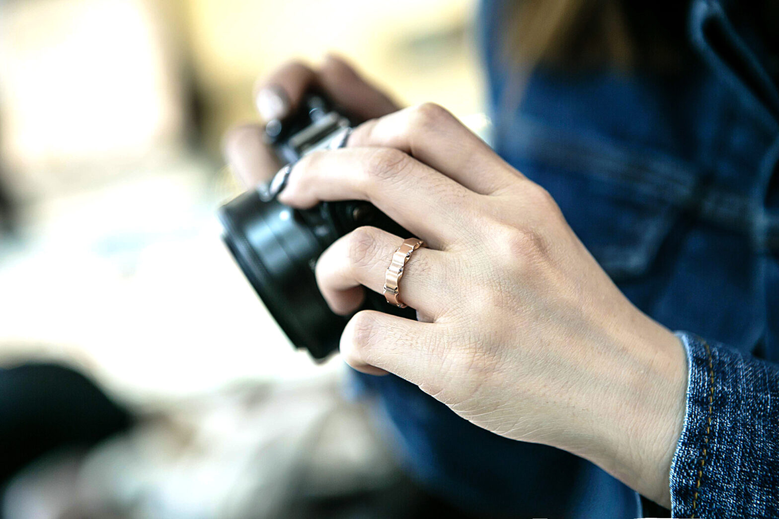 Hand of a female wearing a denim top holding a black camera