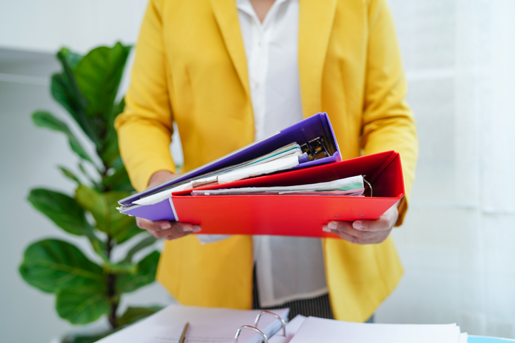 Person wearing yellow jacket holding one purple and one red lever arch folder.