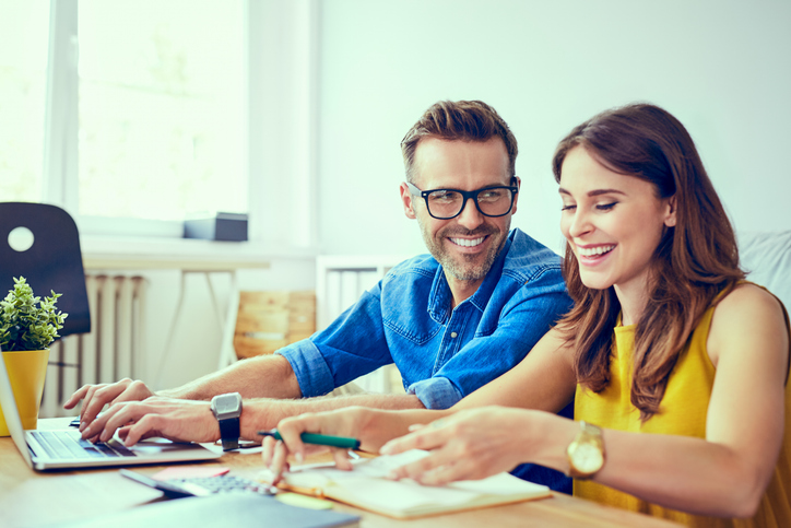 Smiling couple sitting at a table with laptops.