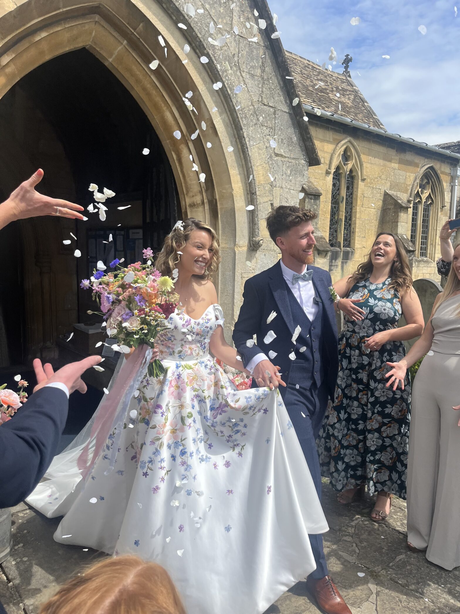 Young couple exiting church on wedding day smiling, holding hands with confetti thrown over them